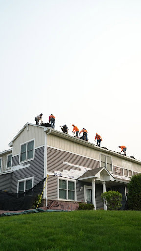 Siding installation in progress on a residential building, showing Tyvek wrap and workers on the roof, by Archcraft Exteriors in South Saint Paul, MN.