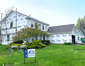A house undergoing siding installation, wrapped in Tyvek, with an A&D Exteriors sign on the lawn in Naperville, IL.