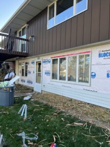 Workers on scaffolding installing light beige siding on the gable end of a house, by DJ Paz All Siding & Roofing Construction in Iowa City, IA