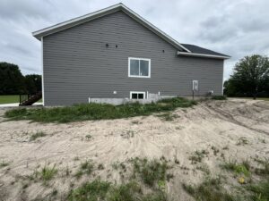 Side view of a house with light beige siding and a wooden deck, showing ongoing siding work by DJ Paz All Siding & Roofing Construction in Iowa City, IA