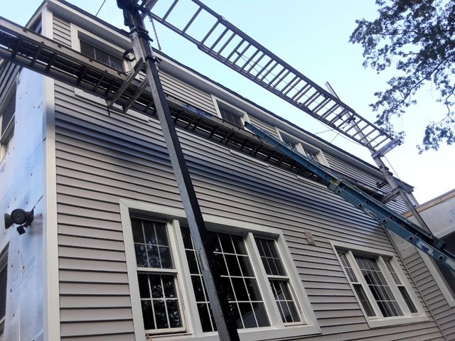 Workers installing light gray horizontal siding on a house using ladders and scaffolding by DL Roofing and Siding in New Haven, CT