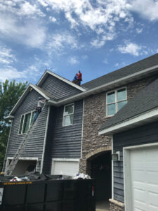 A worker on a ladder installing new siding on a house, demonstrating siding contractor work by Shelter Construction LLC in Brooklyn Park, MN.
