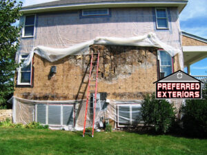 House exterior with old siding removed, exposing plywood sheathing and a ladder, work by Preferred Exteriors in Roswell, GA