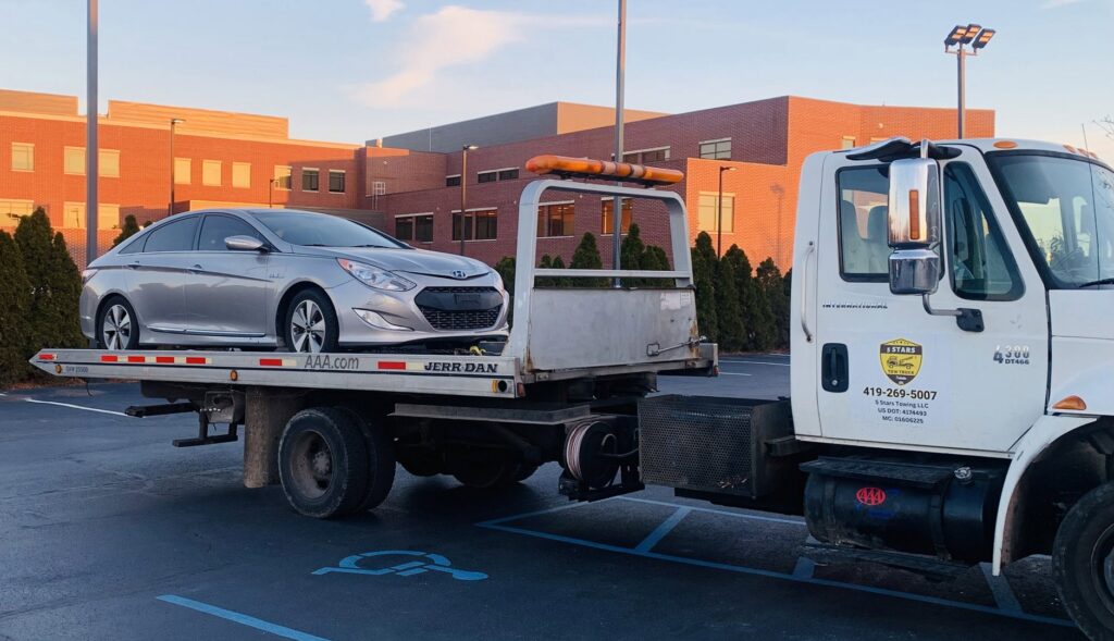 A silver car being transported on a flatbed tow truck by 5 Stars Auto Sales in Toledo, OH.