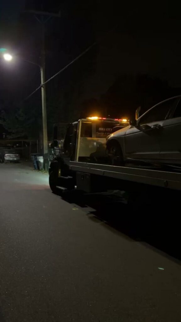 A silver car loaded onto a flatbed tow truck from Bullcity Towing & Services LLC on a street at night in Durham, NC.