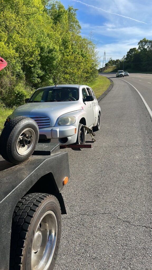 A silver car with a missing front wheel being loaded onto a flatbed tow truck by Tow Truck Company in Johnson City, TN.