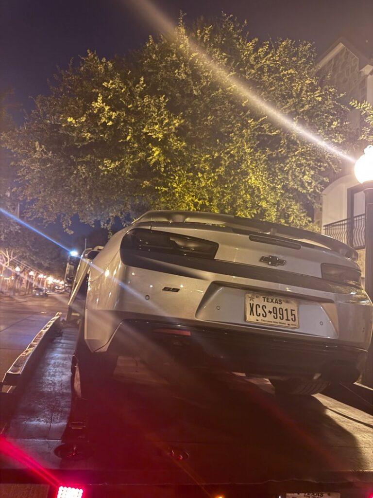 A silver Chevrolet Camaro being transported on a flatbed tow truck at night by Towing Near Me 247 LLC in Irving, TX.