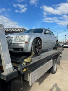A silver Chrysler 300 sedan being transported on a flatbed tow truck by Jay Towing Services in Houston, TX.