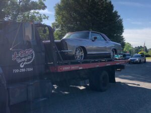 A silver classic car being transported on a flatbed tow truck by A-ROD Towing in Denver, CO.
