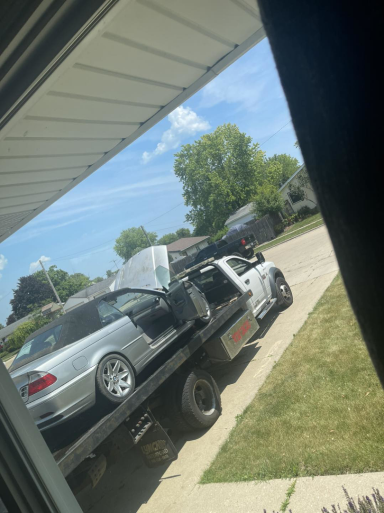 A silver convertible car being transported on a flatbed tow truck by Demand Salvage & Towing in Kenosha, WI.