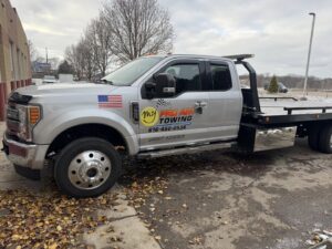 A silver flatbed tow truck with Pro Am Towing branding parked outside Pro Am Collision & Mechanical in Grand Rapids, MI.