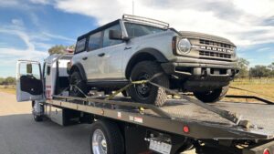 A silver Ford Bronco SUV securely loaded onto a TP Towing flatbed truck for transport in Tampa, FL.