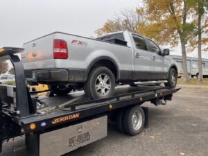 A silver Ford F-150 pickup truck being transported on a flatbed tow truck by Black Mamba Towing & Recovery Llc in Aurora, CO.