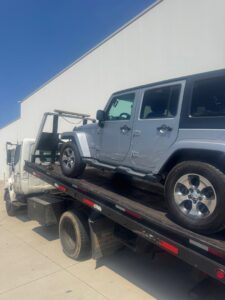 A silver Jeep Wrangler being towed on a flatbed tow truck by Black Rhino Towing in Denver, CO.