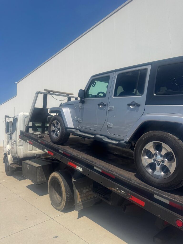 A silver Jeep Wrangler being towed on a flatbed tow truck by Black Rhino Towing in Denver, CO.