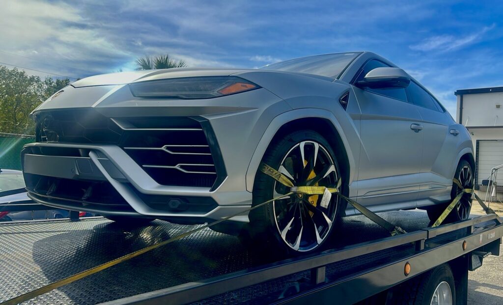 A silver Lamborghini Urus SUV securely loaded onto a TP Towing flatbed truck for luxury vehicle transport in Tampa, FL.