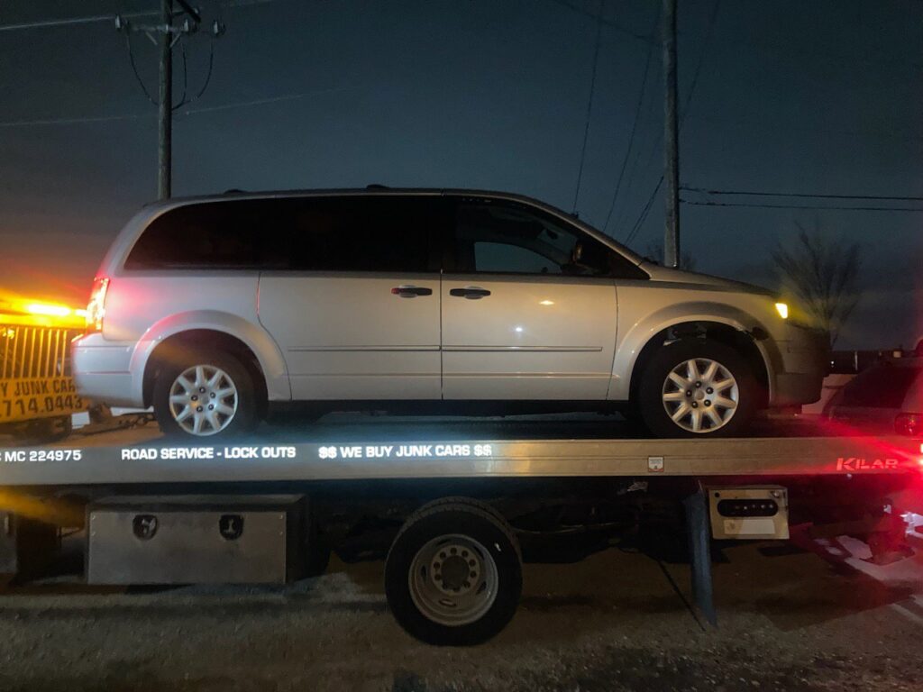 A silver minivan being transported on a flatbed tow truck at night by Towing Recovery Rebuilding Assistance Services in Naperville, IL