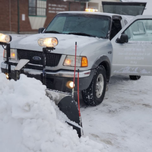 A silver pickup truck with a snow plow actively clearing a pile of snow for Ricky's Snow Removal in Springfield, VA.