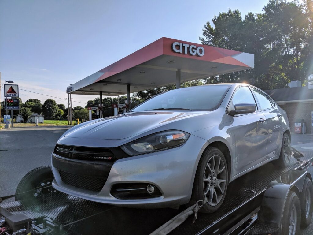 A silver sedan being transported on a car trailer by Snoork Towing, parked at a Citgo gas station in Charlotte, NC.