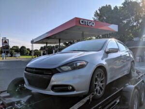 A silver sedan being transported on a car trailer by Snoork Towing, parked at a Citgo gas station in Charlotte, NC.
