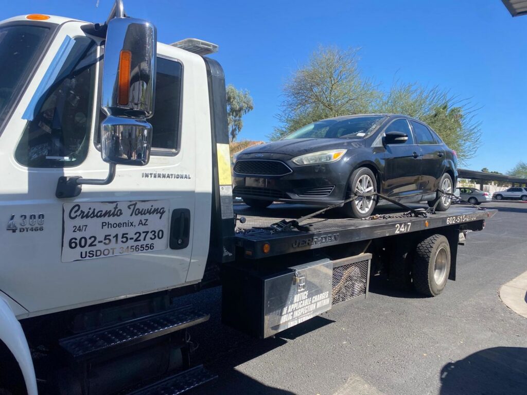 A silver sedan being transported on a flatbed tow truck by Crisanto Towing in Phoenix, AZ.