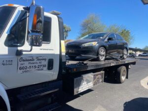 A silver sedan being transported on a flatbed tow truck by Crisanto Towing in Phoenix, AZ.