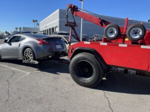 A silver sports car being towed by a red wrecker-style tow truck from Tiki's Towing LLC in Jacksonville, FL.