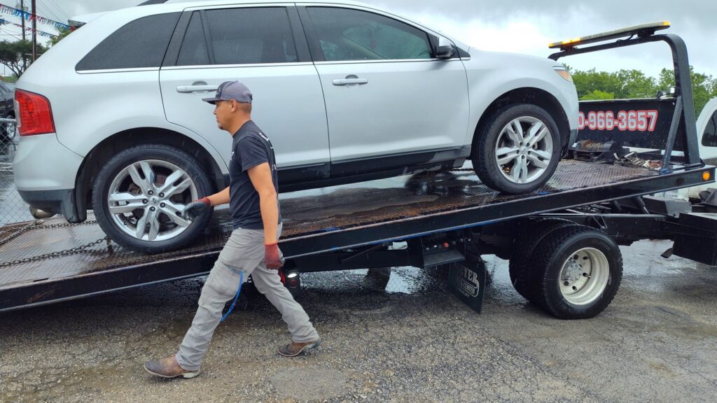 A silver SUV being loaded onto a flatbed tow truck in a parking lot by AB Towing & Transport in San Antonio, TX.