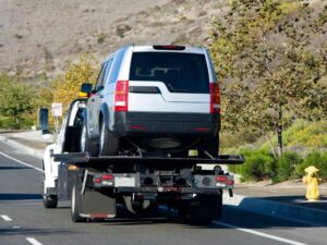 A silver SUV being transported on a white flatbed tow truck on a highway by Spokane Towing Services in Spokane, WA.
