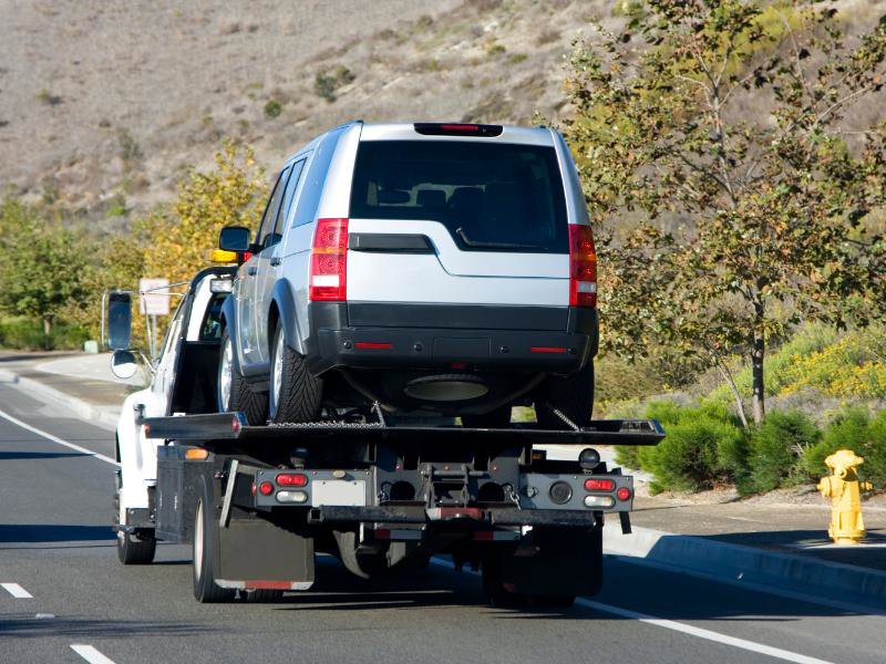 A silver SUV being transported on a white flatbed tow truck on a highway by Spokane Towing Services in Spokane, WA.
