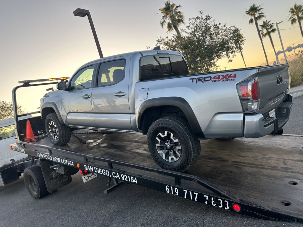 A silver Toyota Tacoma pickup truck being transported on a flatbed tow truck by Cali kings Towing in San Diego, CA.