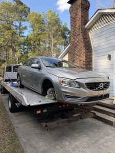 A silver Volvo sedan with a missing front wheel being loaded onto a flatbed tow truck by Bullcity Towing & Services LLC in Durham, NC.