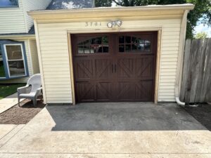 A single brown garage door with arched windows and decorative hardware installed by Woodwards Overhead Door Co. in Topeka, KS