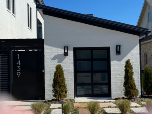 A single modern black glass garage door on a white brick house, installed by Garage Door Sales & Repair in Conway, AR.