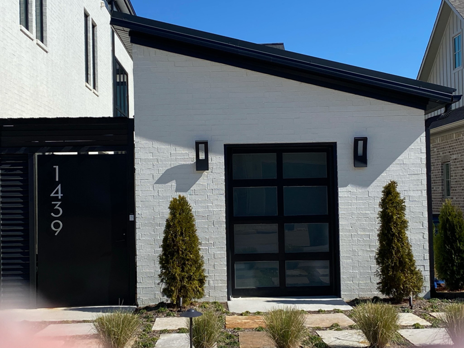 A single modern black glass garage door on a white brick house, installed by Garage Door Sales & Repair in Conway, AR.