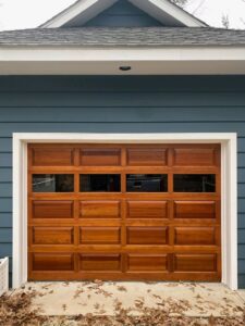 A single wooden-style garage door with windows installed on a blue-sided house by Hickman Overhead Door in Milford, DE.