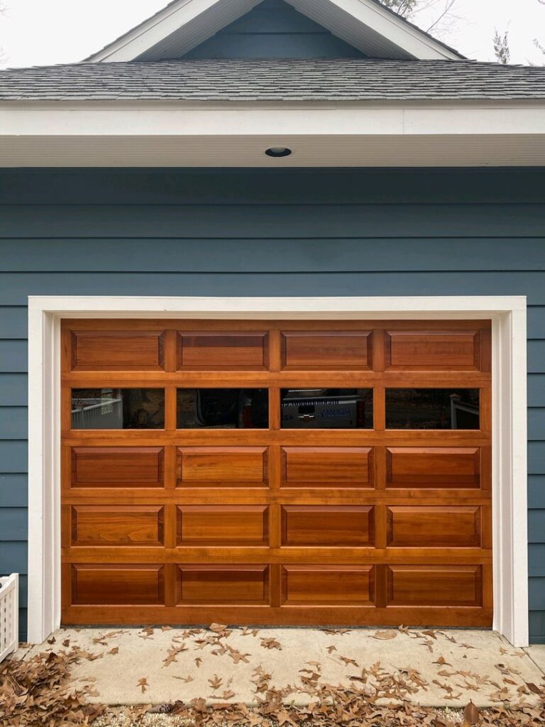 A single wooden-style garage door with windows installed on a blue-sided house by Hickman Overhead Door in Milford, DE.