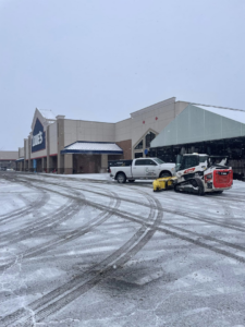 A Bobcat skid steer and a pickup truck with plows clearing snow from a Lowe's parking lot for Cities Lawn and Snow LLC in Woodbury, MN.