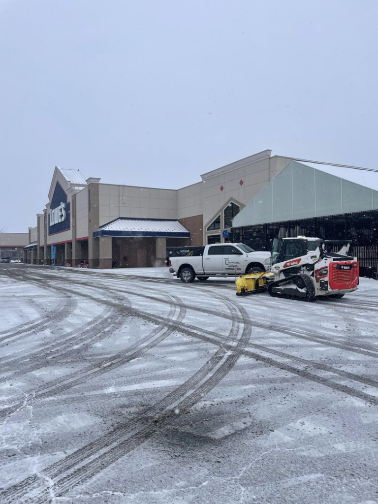 A Bobcat skid steer and a pickup truck with plows clearing snow from a Lowe's parking lot for Cities Lawn and Snow LLC in Woodbury, MN.