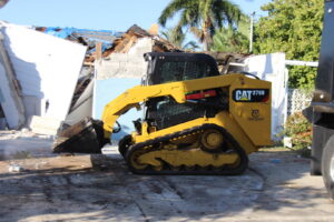 A skid steer clearing demolition debris from a partially demolished structure by New Wave Concepts in Cape Coral, FL.