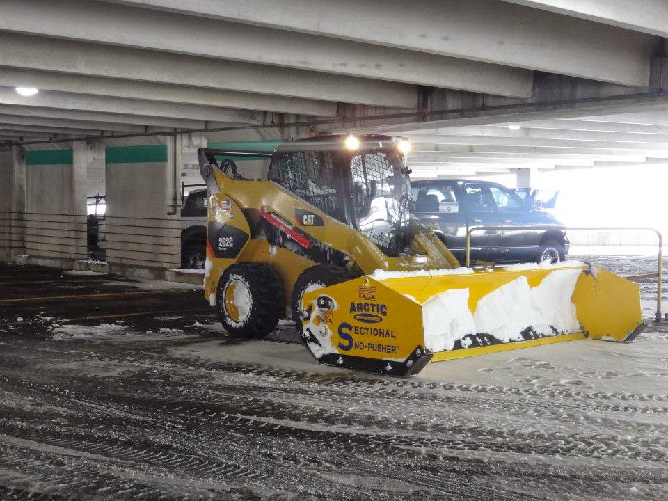 A yellow skid steer with a snow pusher attachment clearing snow from a parking garage by The Groundskeeper Inc. in Fort Collins, CO.