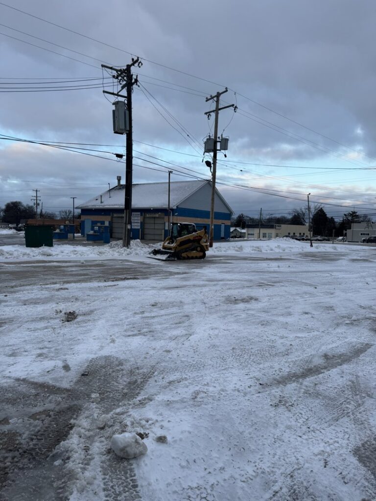 A skid steer loader clearing snow from a commercial parking lot, provided by Luna Landscape Pro in Racine, WI.