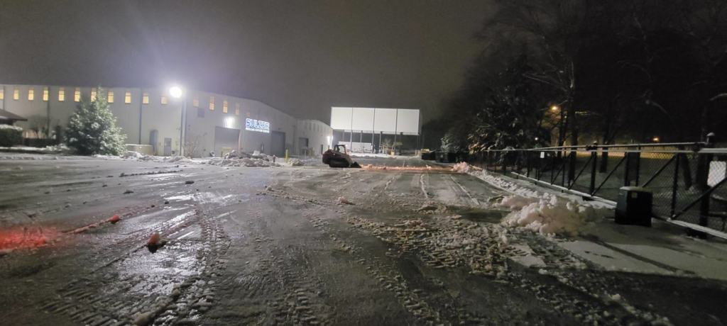 A skid steer actively clearing snow from a commercial parking lot at night by Yard Monkeys in Hixson, TN.