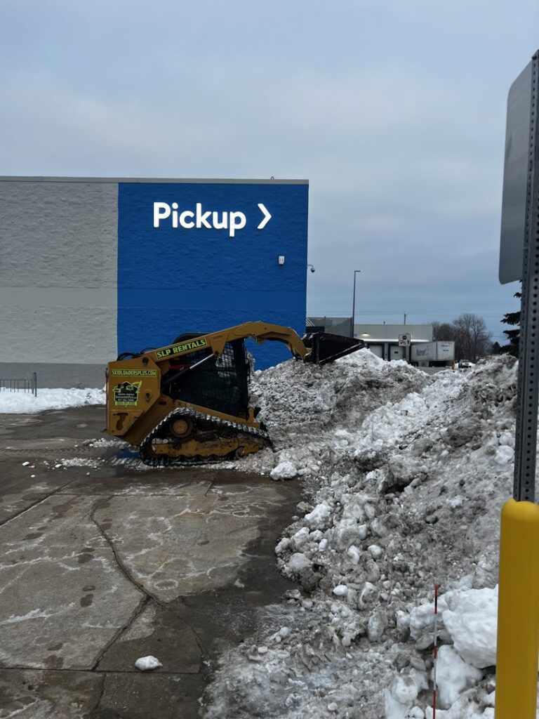 A yellow skid steer loader actively piling snow in a commercial parking lot for Appleton Snow Removal in Appleton, WI.