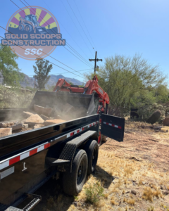 A skid steer loader efficiently loading demolition debris into a dump trailer for Solid Scoops Construction in Tucson, AZ.