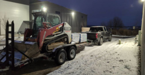 A skid steer loaded on a trailer, towed by a truck on a snowy night for Creative Grounds in Springdale, AR