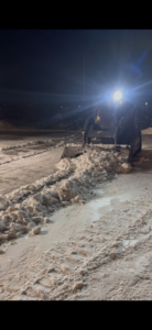 A skid steer with a plow attachment actively clearing snow from a parking lot at night by OnPoint Land Solutions, LLC in Enid, OK.