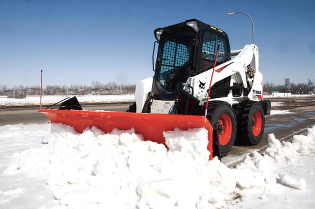 A Bobcat skid-steer loader with a snow plow clearing snow for Landscapes plus in Oklahoma City, OK.