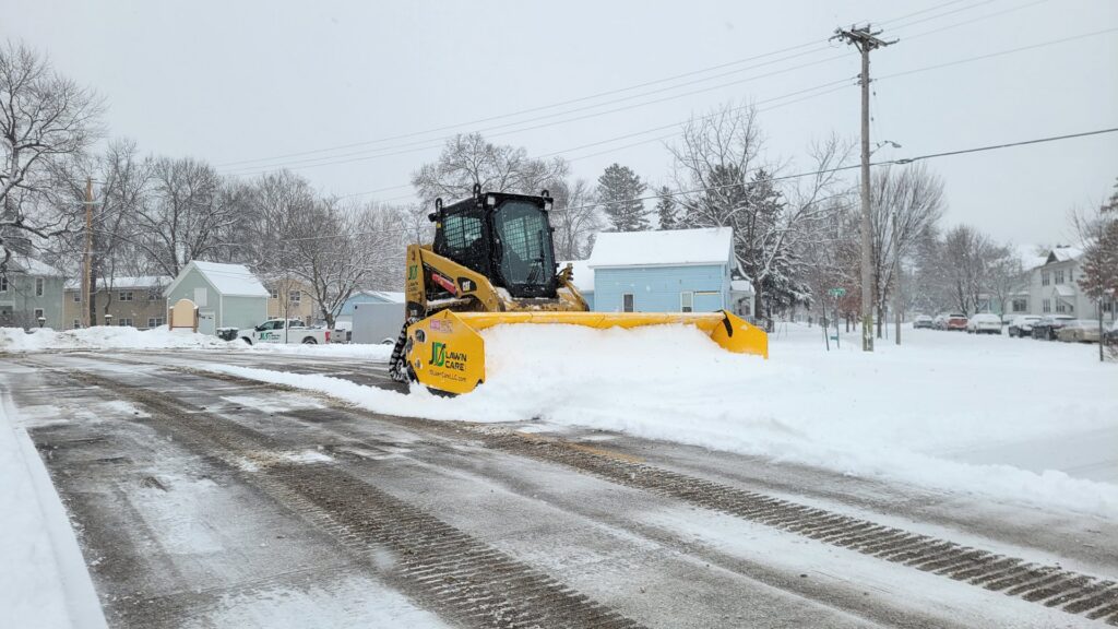 A JD Lawn Care LLC skid steer with a snow pusher attachment clearing a snowy street in Berea, OH.