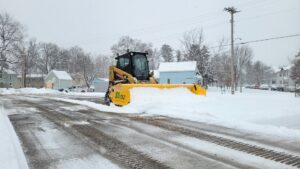 A JD Lawn Care LLC skid steer with a snow pusher attachment clearing a snowy street in Berea, OH.